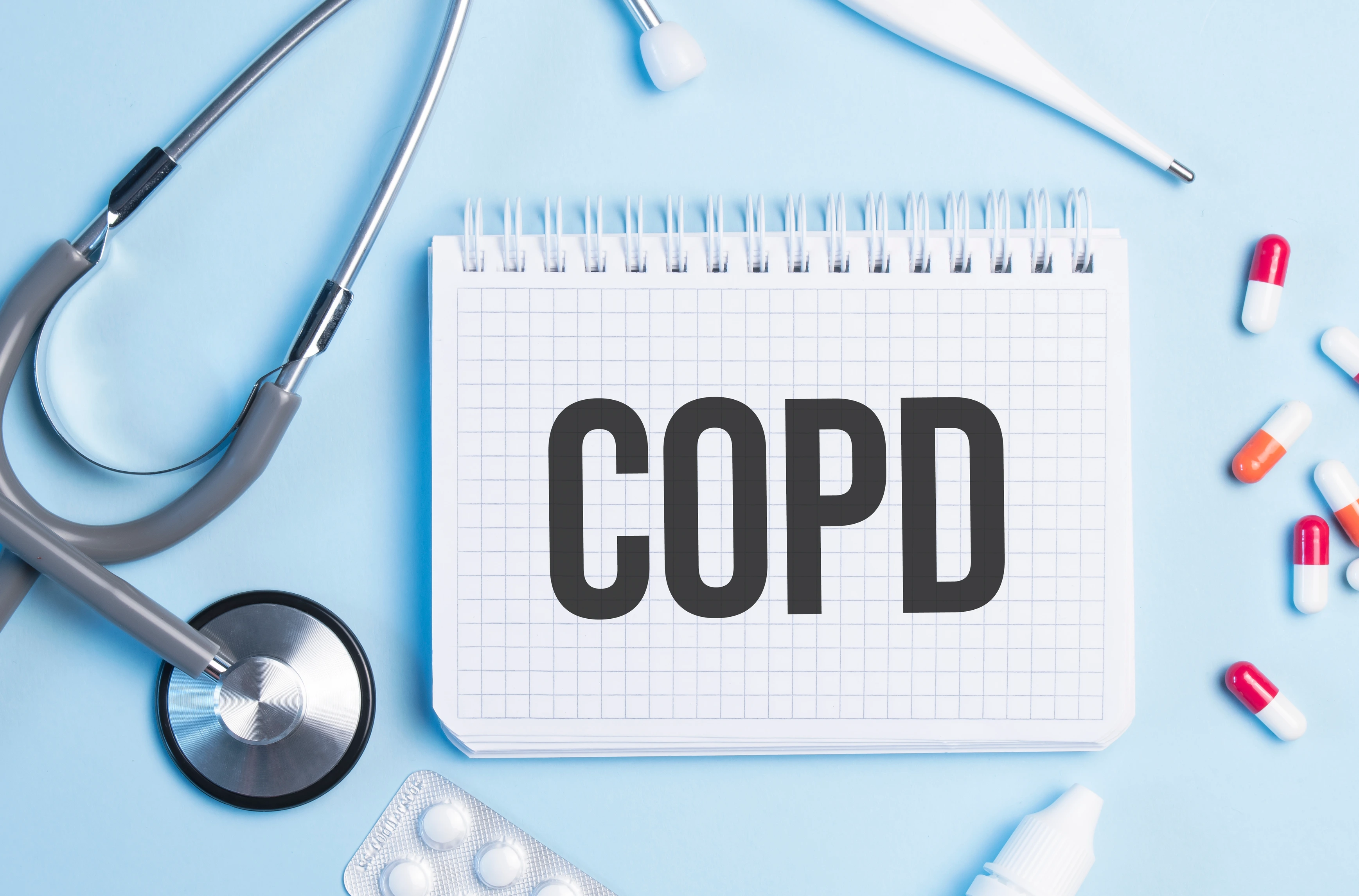 The word copd written on a white notepad on a blue background near a stethoscope, syringe, electronic thermometer and pills. Medical concept