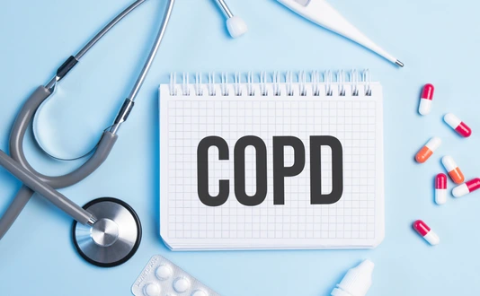The word copd written on a white notepad on a blue background near a stethoscope, syringe, electronic thermometer and pills. Medical concept