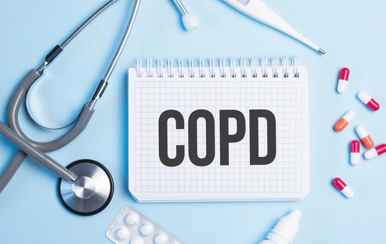 The word copd written on a white notepad on a blue background near a stethoscope, syringe, electronic thermometer and pills. Medical concept