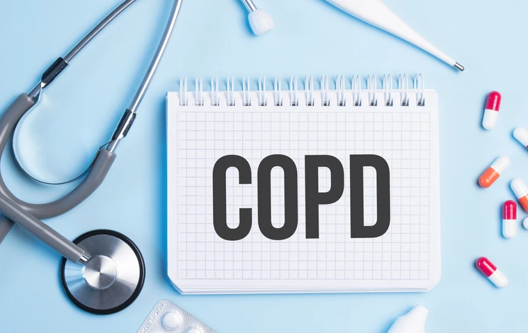The word copd written on a white notepad on a blue background near a stethoscope, syringe, electronic thermometer and pills. Medical concept