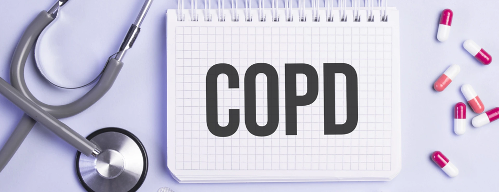 The word copd written on a white notepad on a blue background near a stethoscope, syringe, electronic thermometer and pills. Medical concept
