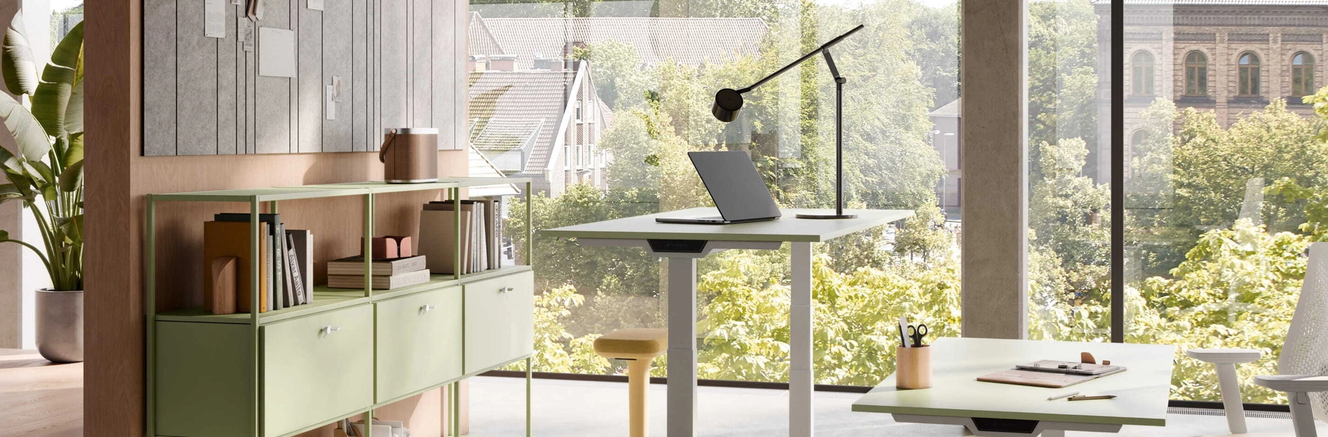 Ein höhenverstellbarer Schreibtisch vor einem Raumtrenner mit Kommode in einem warm und offen eingerichtetem Büro.