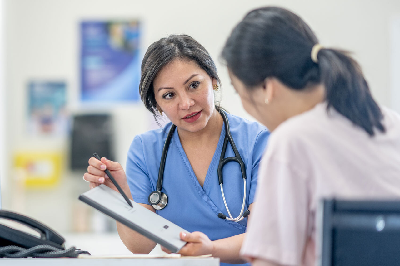 Eine Pflegefachperson erkärt einer Patientin etwas, sie hat ein Klemmbrett in der Hand, auf dem sie etwas zeigt.