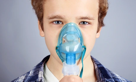 Young boy using nebulizer for asthma and respiratory diseases on light background