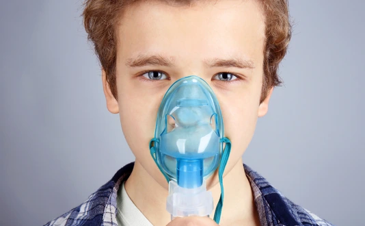 Young boy using nebulizer for asthma and respiratory diseases on light background