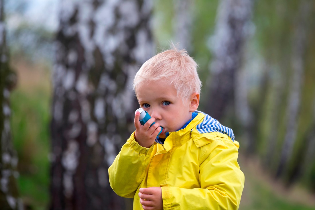 young boy using an asthma inhaler outdoors