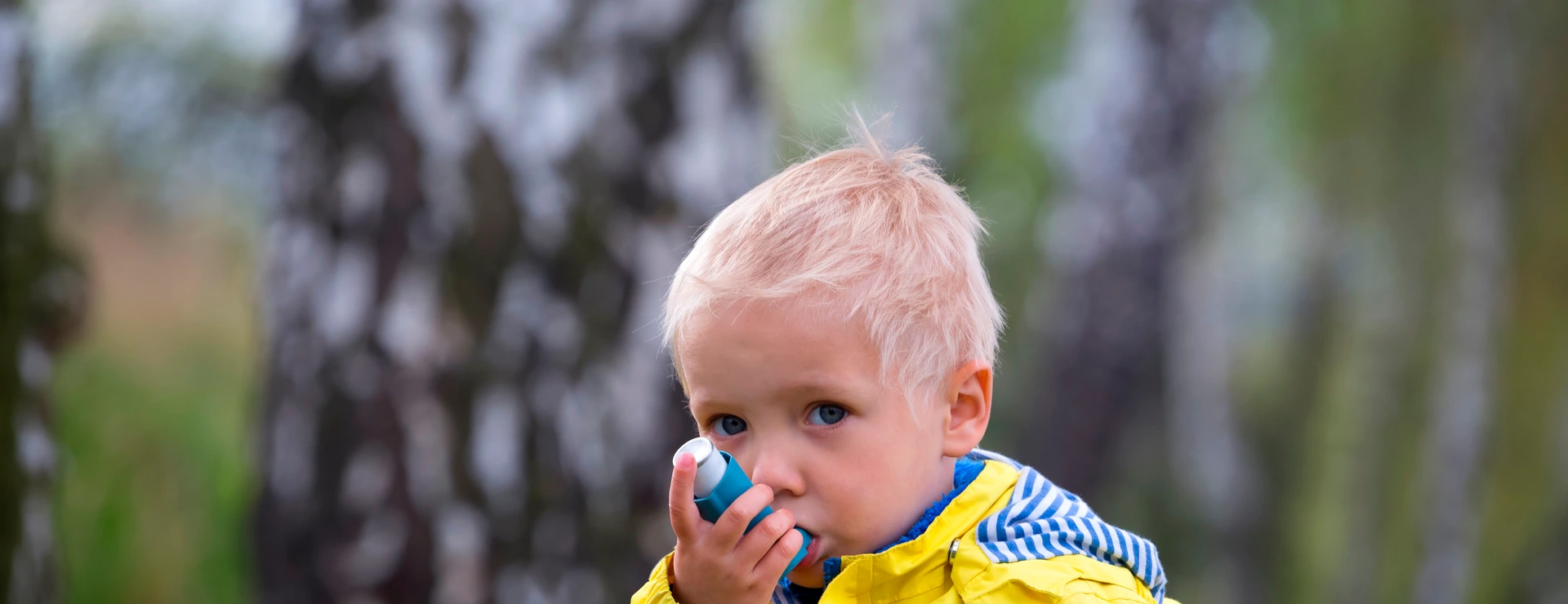 young boy using an asthma inhaler outdoors