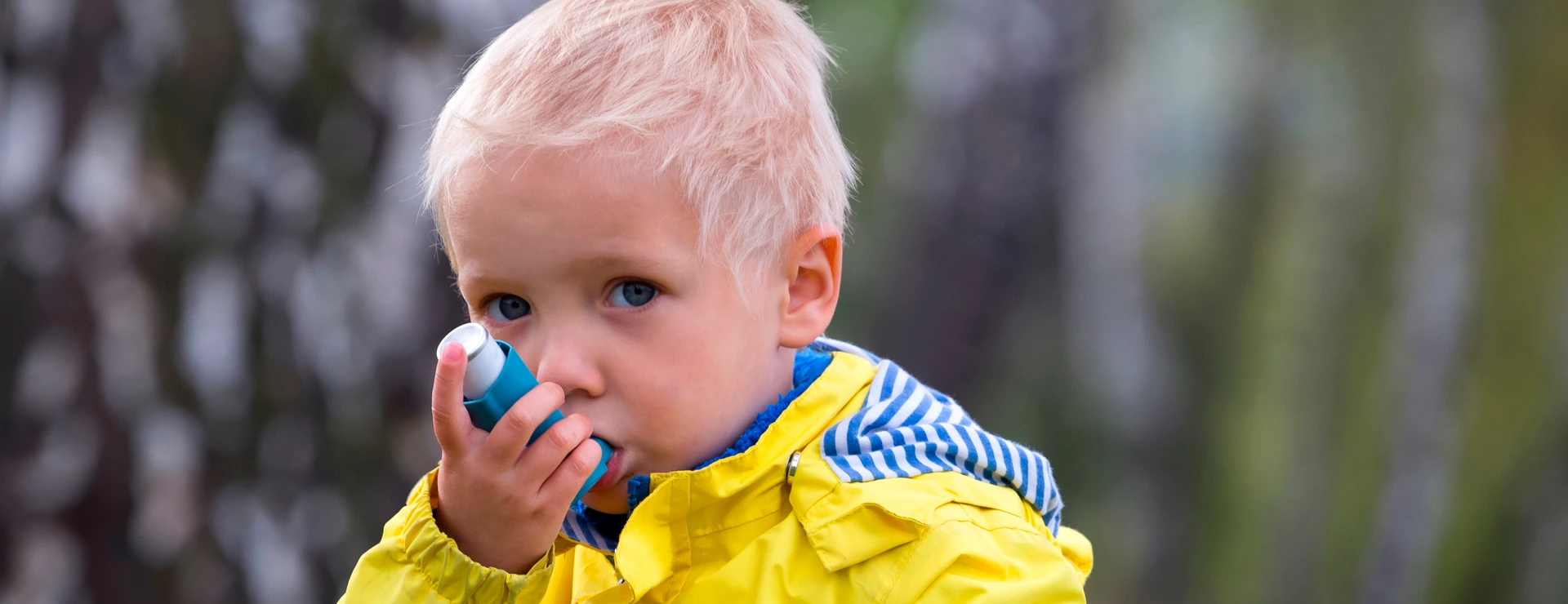 young boy using an asthma inhaler outdoors