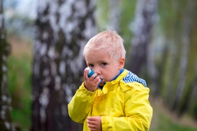 young boy using an asthma inhaler outdoors