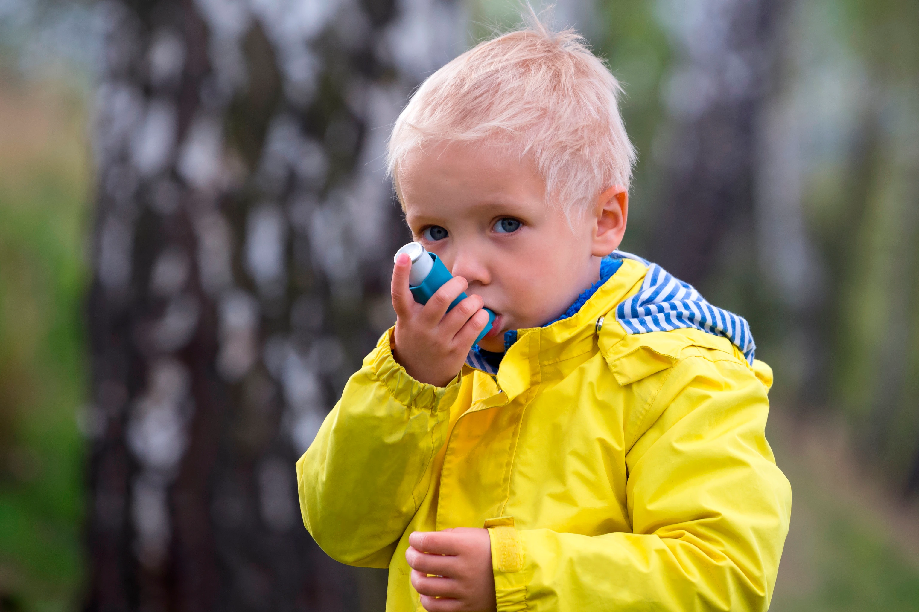 young boy using an asthma inhaler outdoors