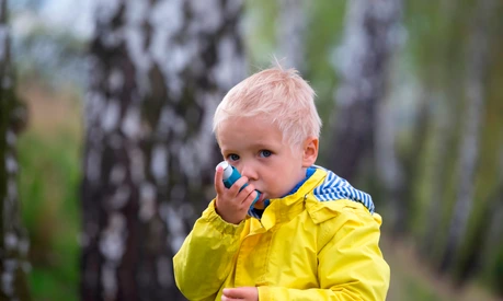 young boy using an asthma inhaler outdoors