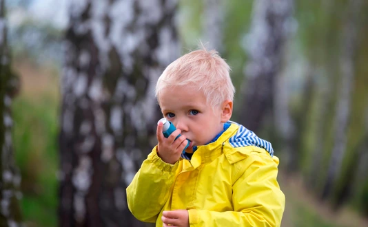 young boy using an asthma inhaler outdoors