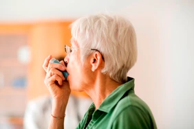 White-haired senior woman using inhaler