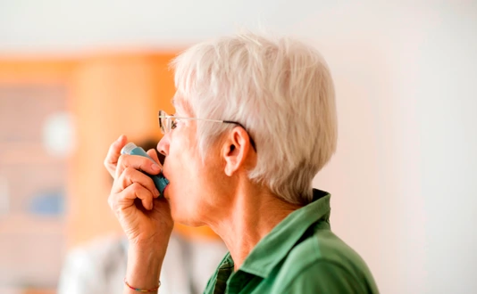 White-haired senior woman using inhaler