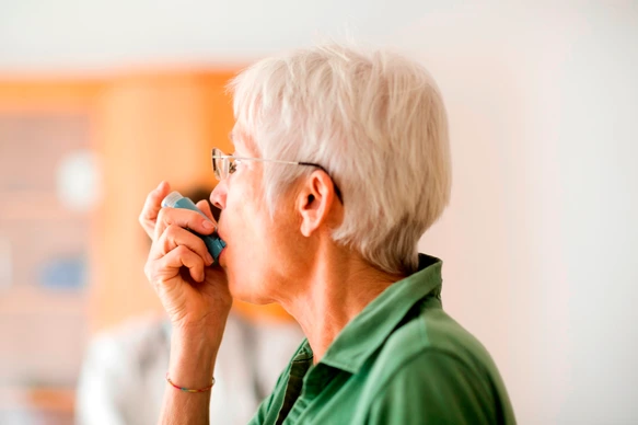 White-haired senior woman using inhaler