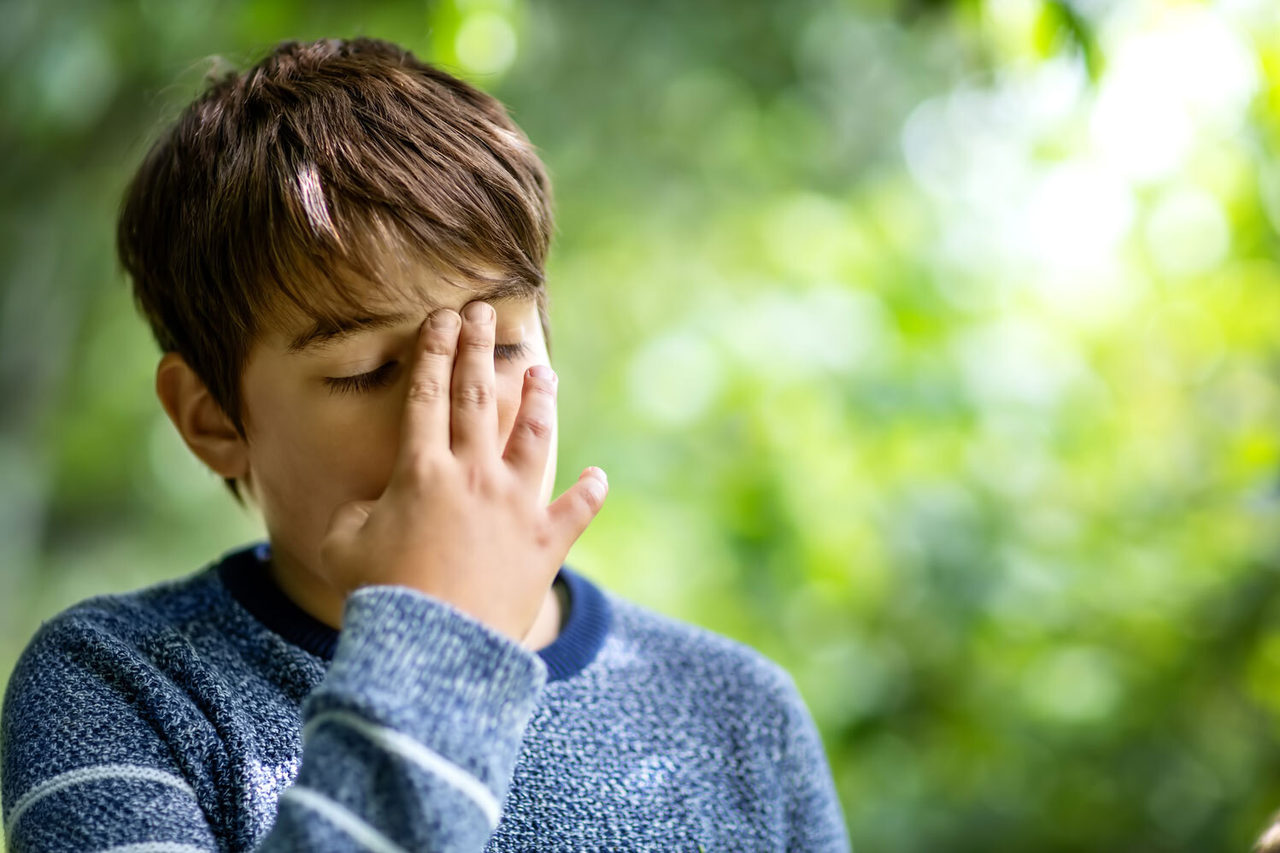 Junge hält sich Hand vor Gesicht leidet unter rätselhaften neurologischen Phänomenen, FNS