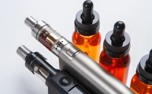 Silver and black vapes next to the vials. Liquids for electronic cigarettes. Smoking e-cigarettes. Vaping accessories. Devices for Smoking electronic cigarettes.