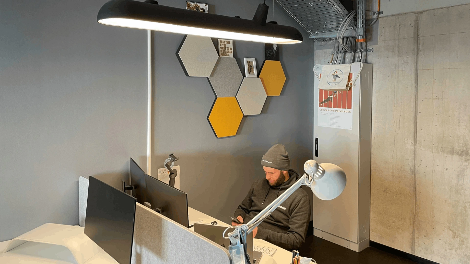 Person sitzt am Arbeitsplatz in kleinem Büro mit PALMBERG-Schreibtisch und Poster CHECK YOUR PRIVILEGES