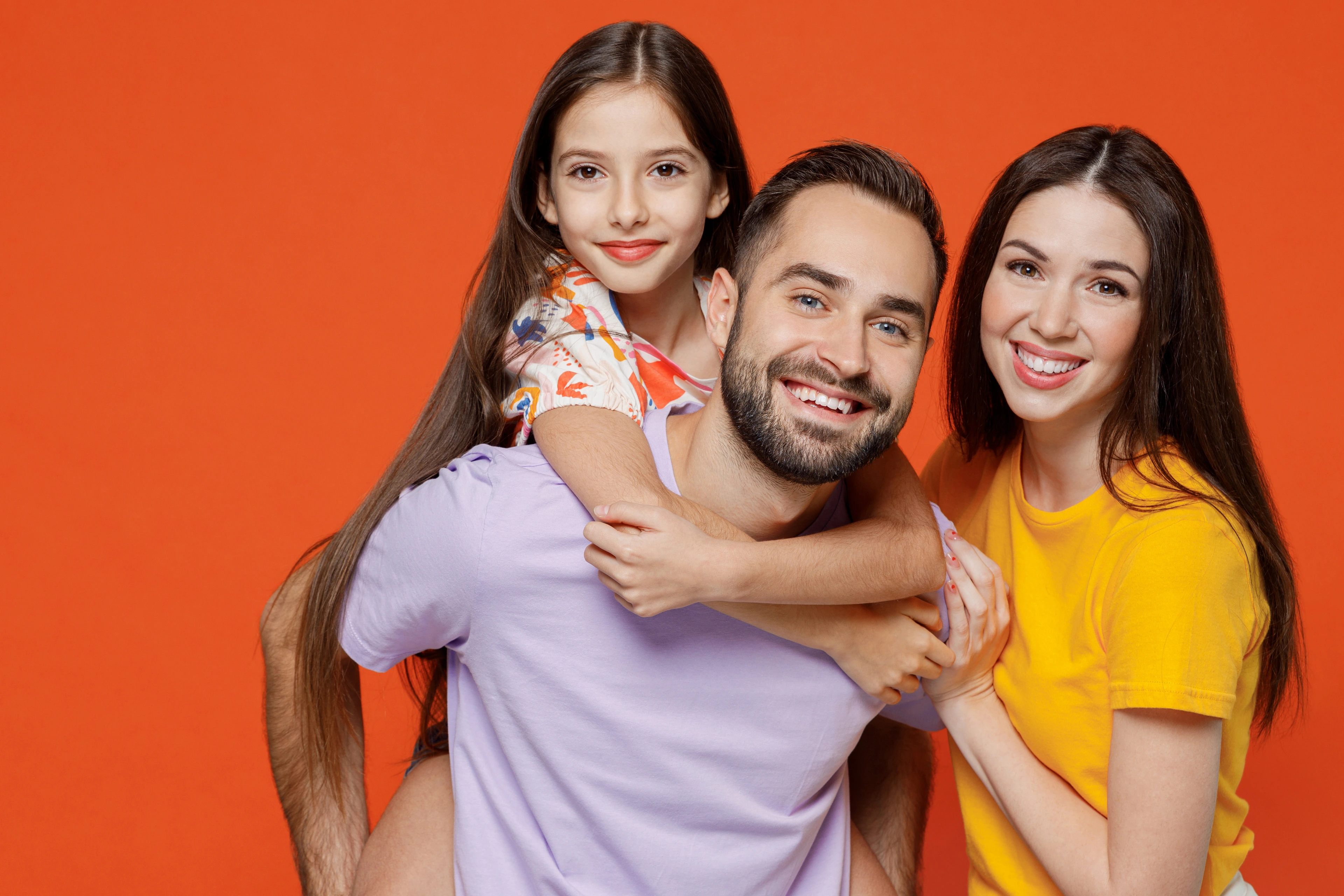 Young fun happy parents mom dad with child kid daughter teen girl in basic t-shirts giving piggyback to daughter isolated on yellow background studio portrait. Family day parenthood childhood concept