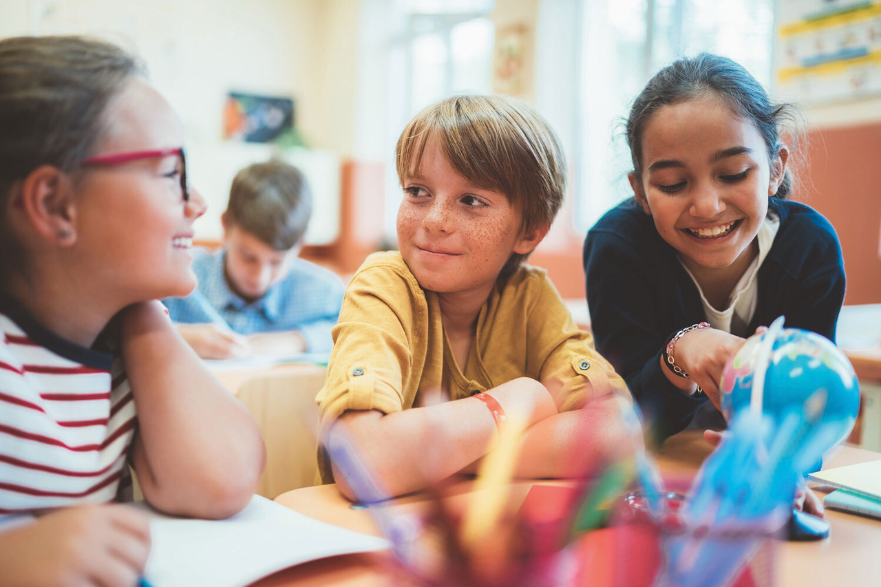 Fröhliche Schülerinnen und Schüler in einem Klassenraum, sie arbeiten selbstständig an verschiedenen Plätzen in Gruppen