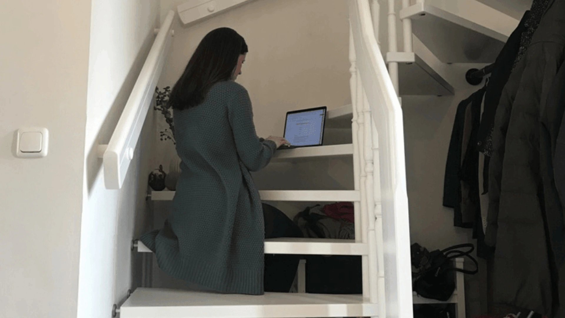 Frau kniet auf weißen Treppen und arbeitet am Laptop im Flur neben einer PALMBERG-Garderobe