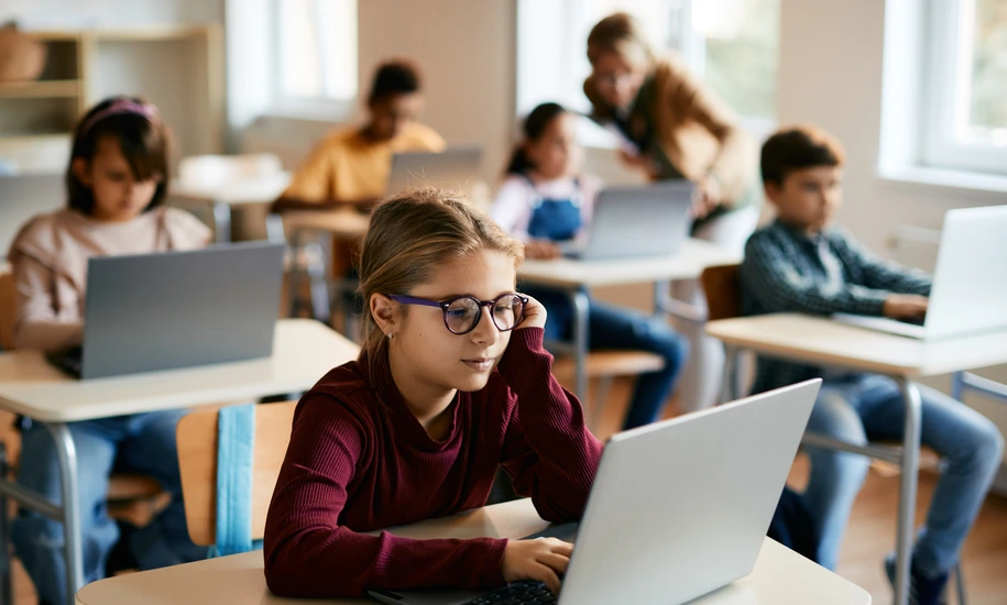 Little girl e-learns on laptop in computer science classroom at elementary school.