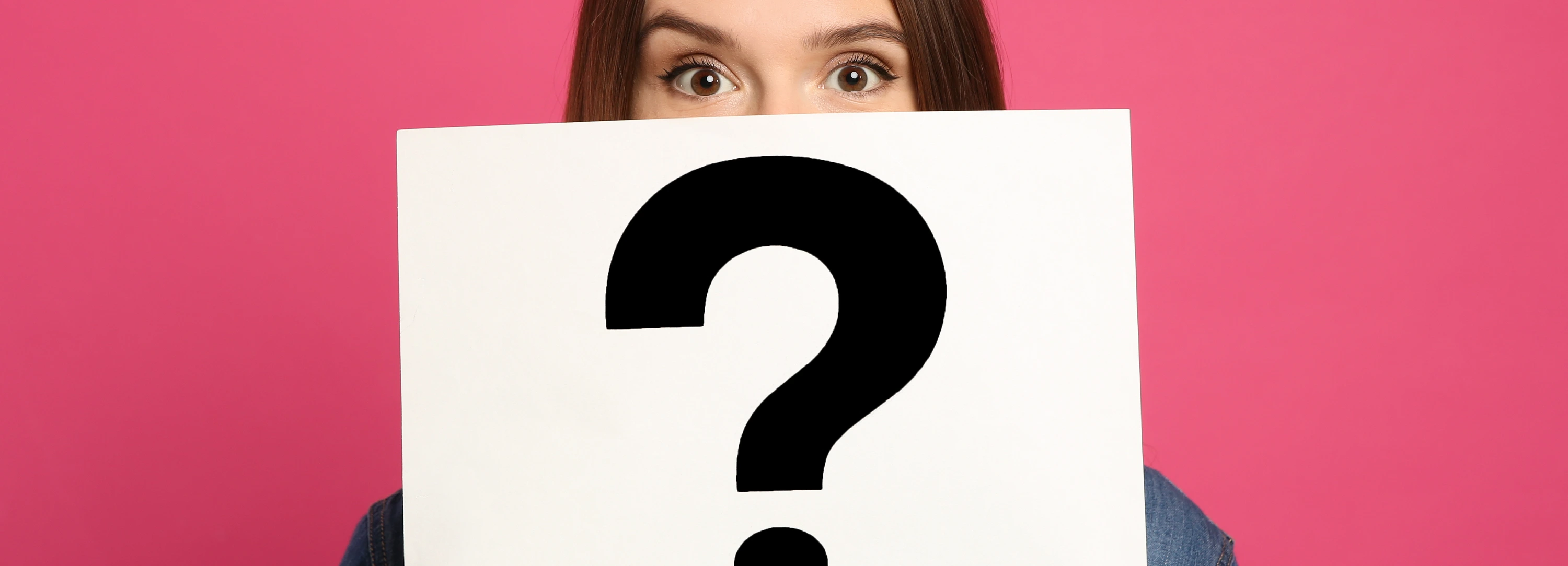 Emotional woman holding question mark sign on pink background