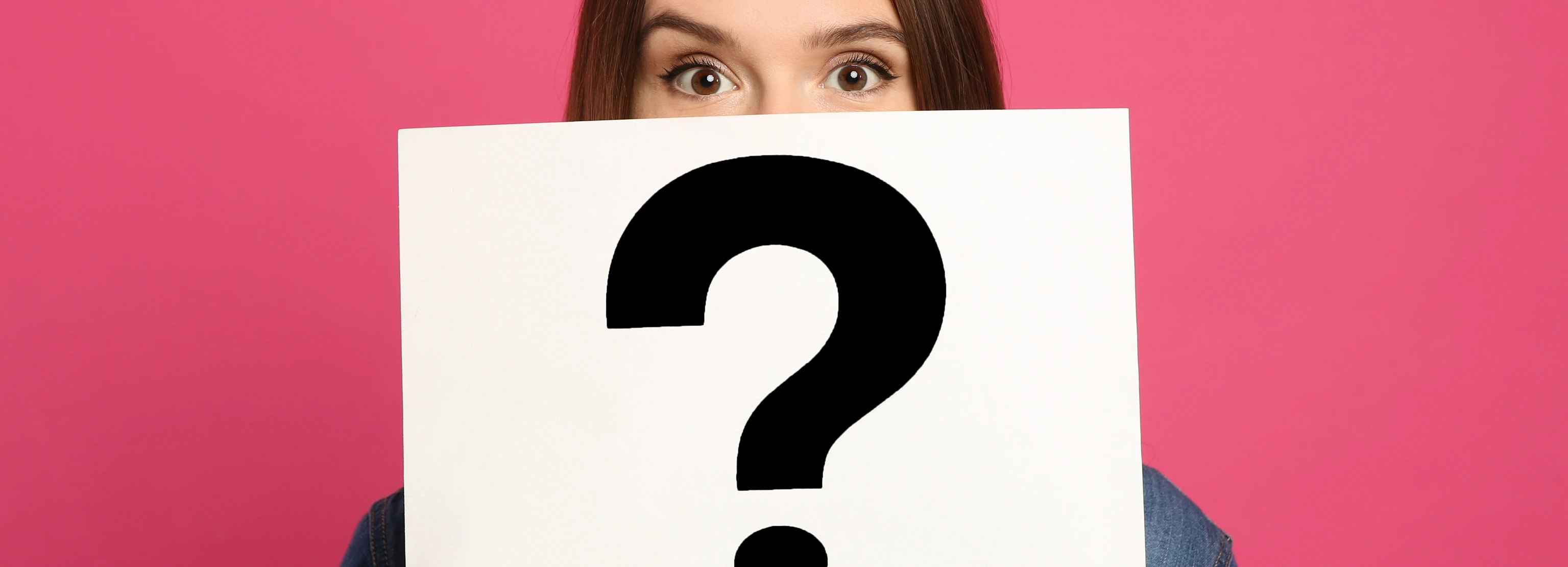 Emotional woman holding question mark sign on pink background