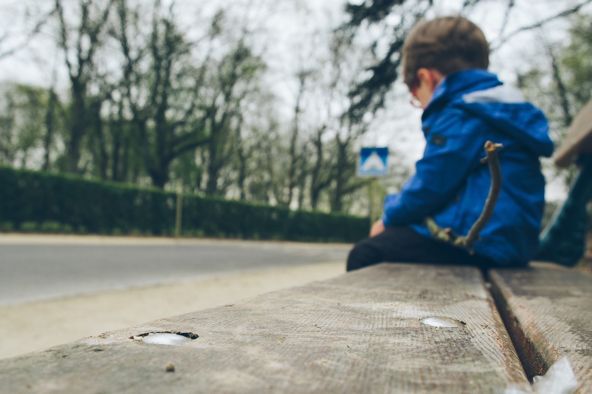 Kleiner Junge in blauer Jacke sitzt auf einer Parkbank.
