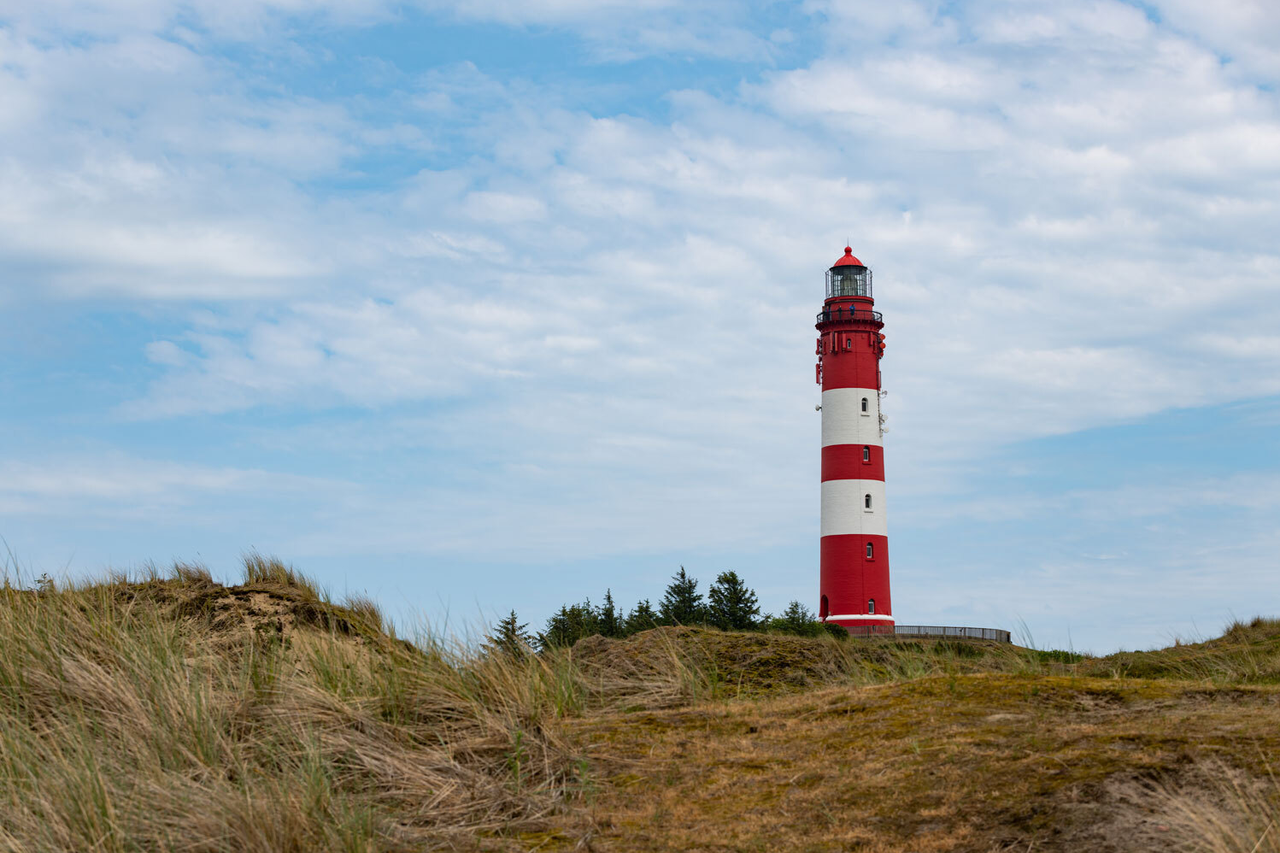 Ein Foto eines rot-weißen Leuchtturms vor einem blauen Himmel mit einigen Wolken