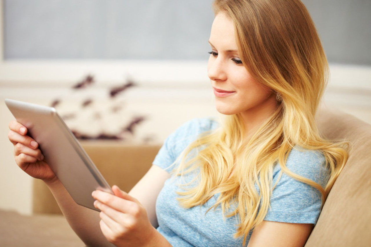 Blonde Frau die auf einem Tablet liest