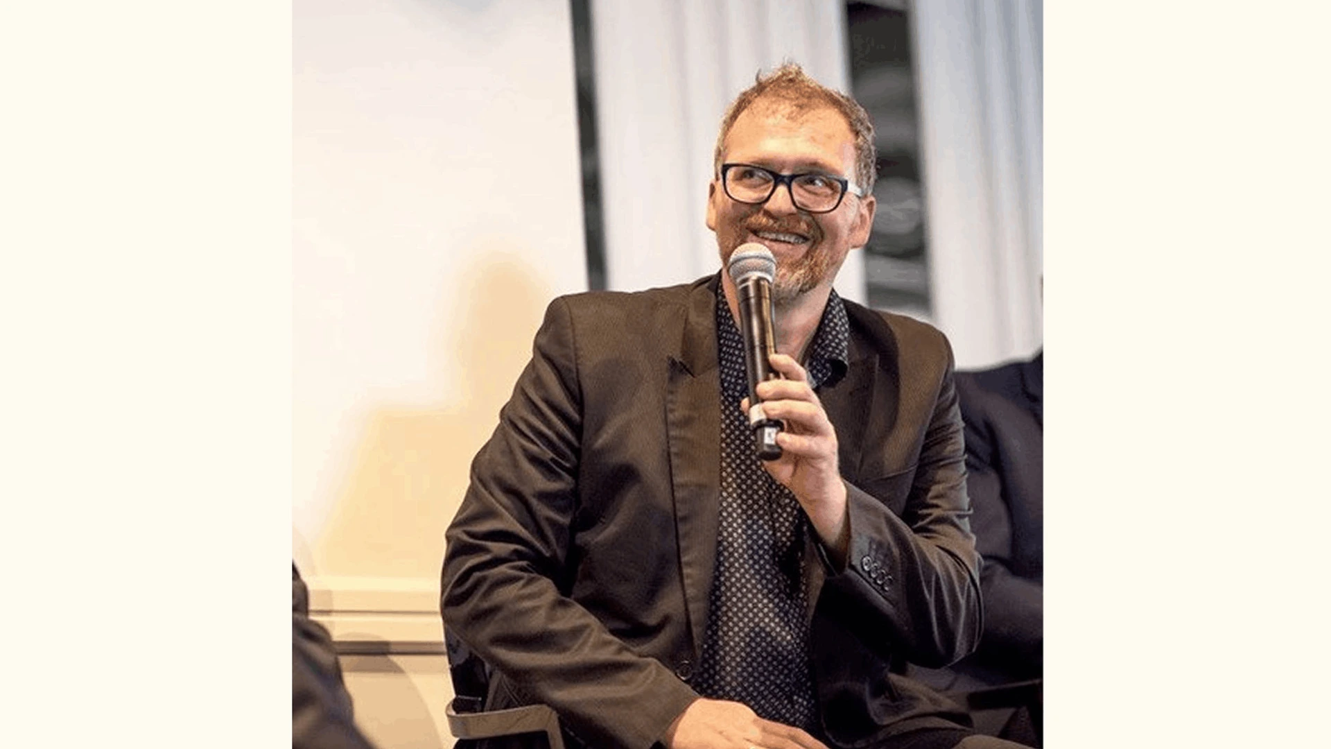 Mann mit Brille hält Mikrofon und lächelt bei einer Diskussionsrunde auf einer PALMBERG-Veranstaltung
