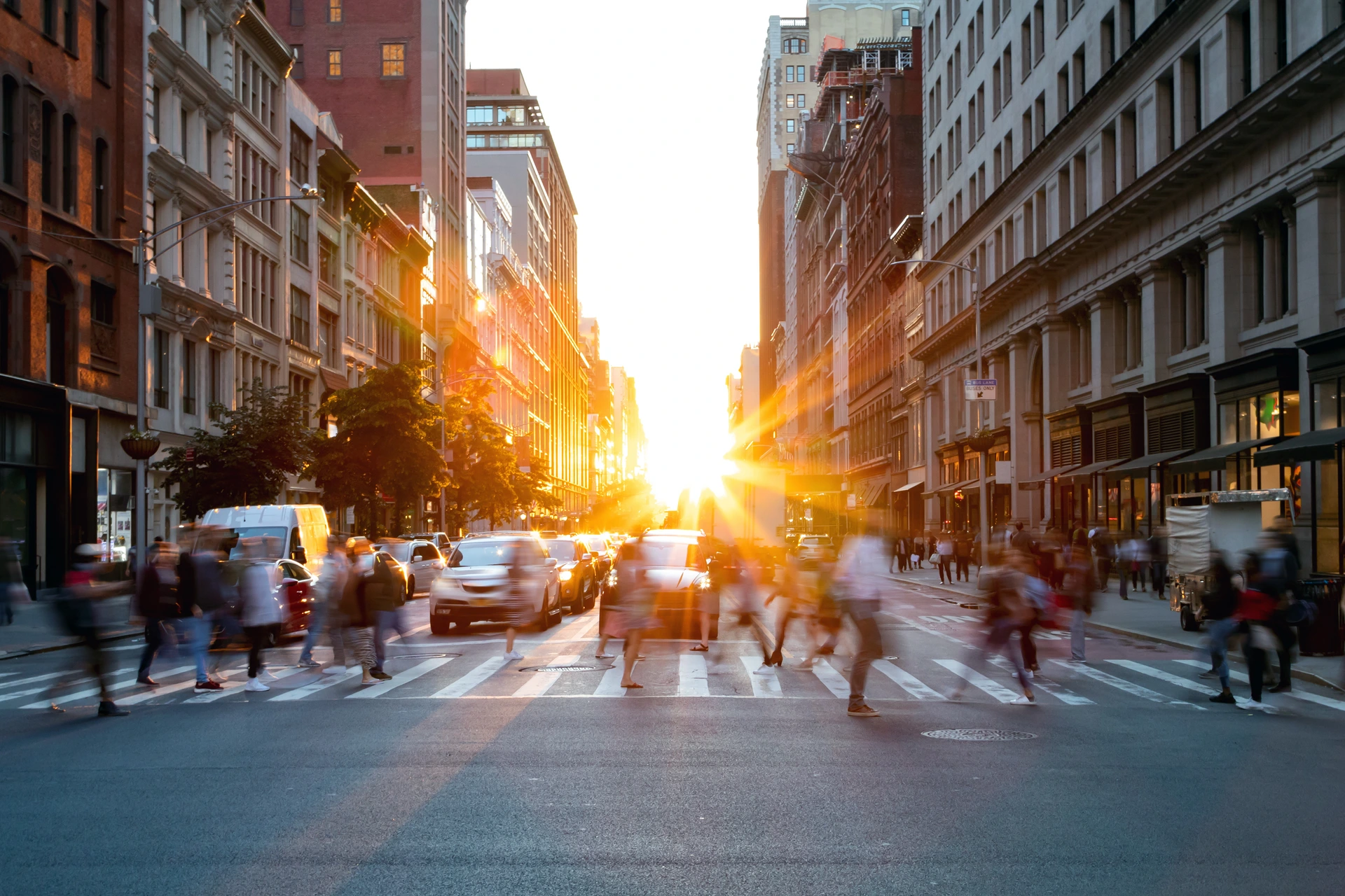 Crowds of busy people walking through the intersection of 5th Avenue and 23rd Street in Manhattan, New York City with bright sunset background