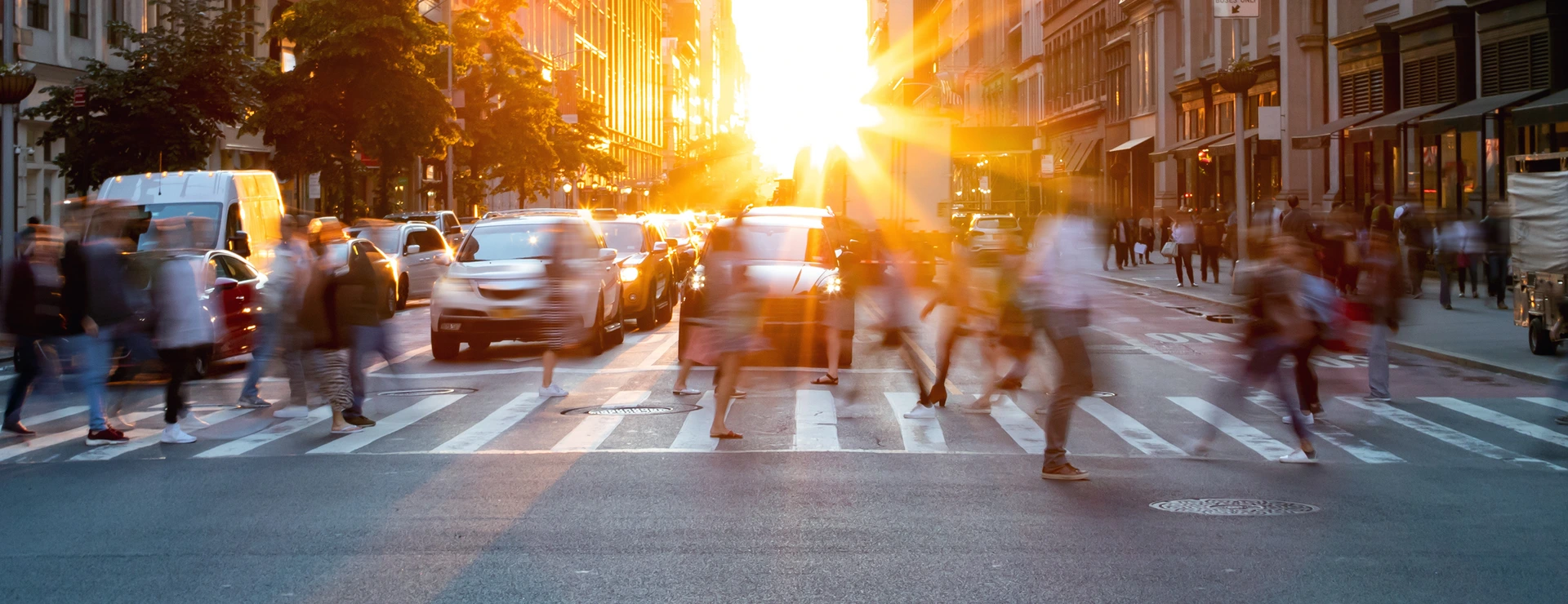 Crowds of busy people walking through the intersection of 5th Avenue and 23rd Street in Manhattan, New York City with bright sunset background
