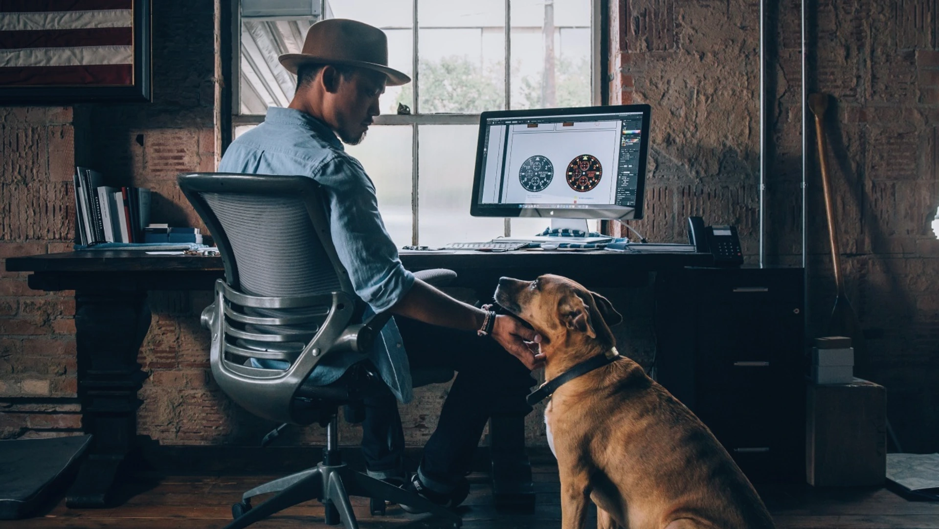 Ein Hund im Home Office an einem Schreibtisch mit einem Mann mit Hut.