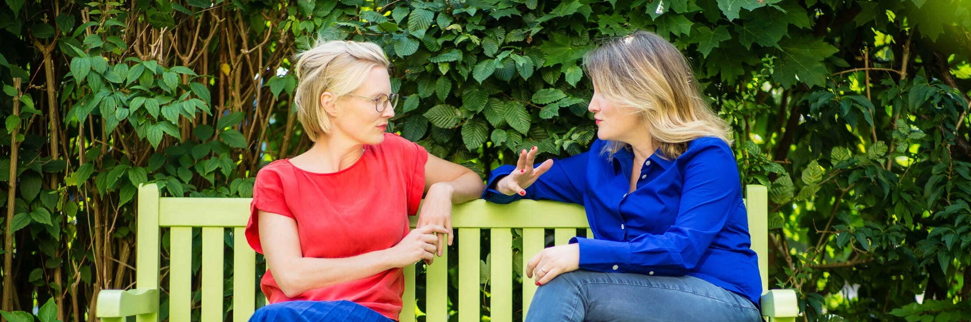 Zwei Frauen sitzen auf einer hellgrünen PALMBERG-Bank im Garten und unterhalten sich.
