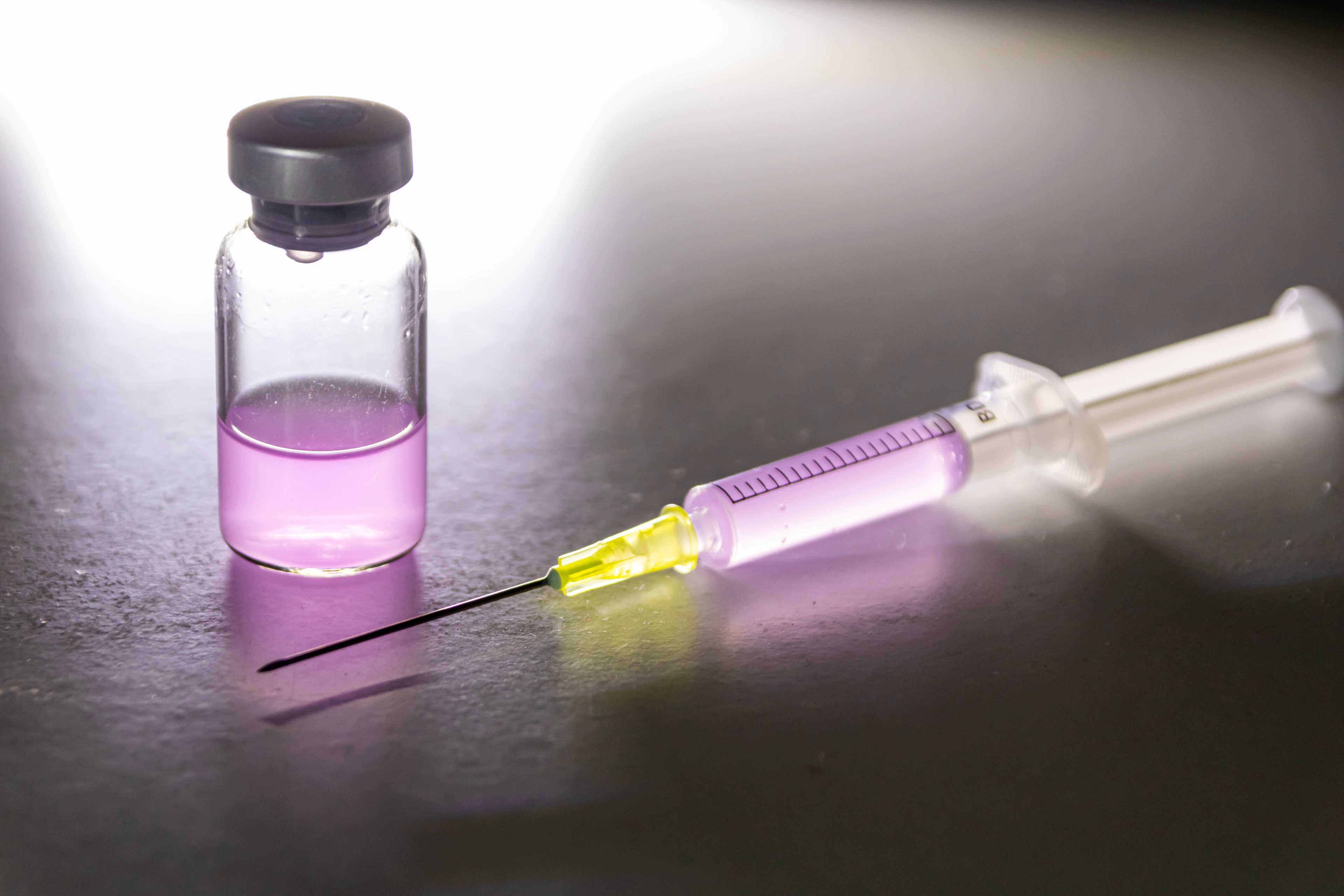 Leuchtende Spritze mit pinkfarbenem Heilmittel aus einer medizinischen Ampulle zur Therapie von Patienten mit Impfstoff und neuartigen Wirkstoffen