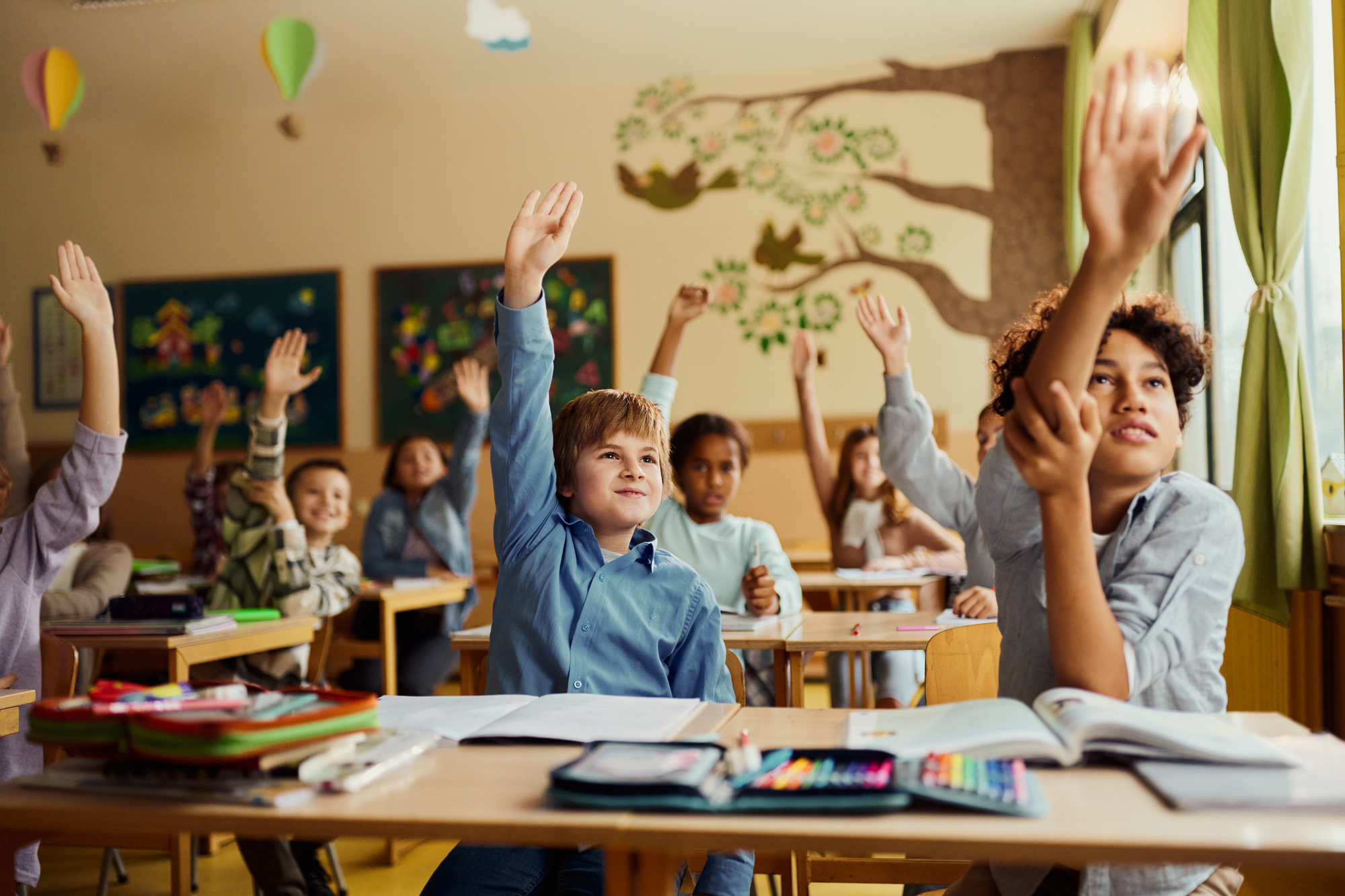 Lächelnde Grundschüler, die ihre Hände heben, um sich zu melden