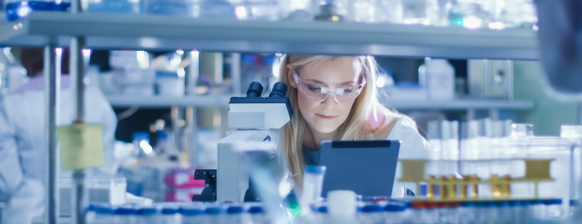 Research Female Scientist is using a Microscope and a Tablet Computer while Working in a Modern Laboratory. Doing Genetic and Pharmaceutical Researches.