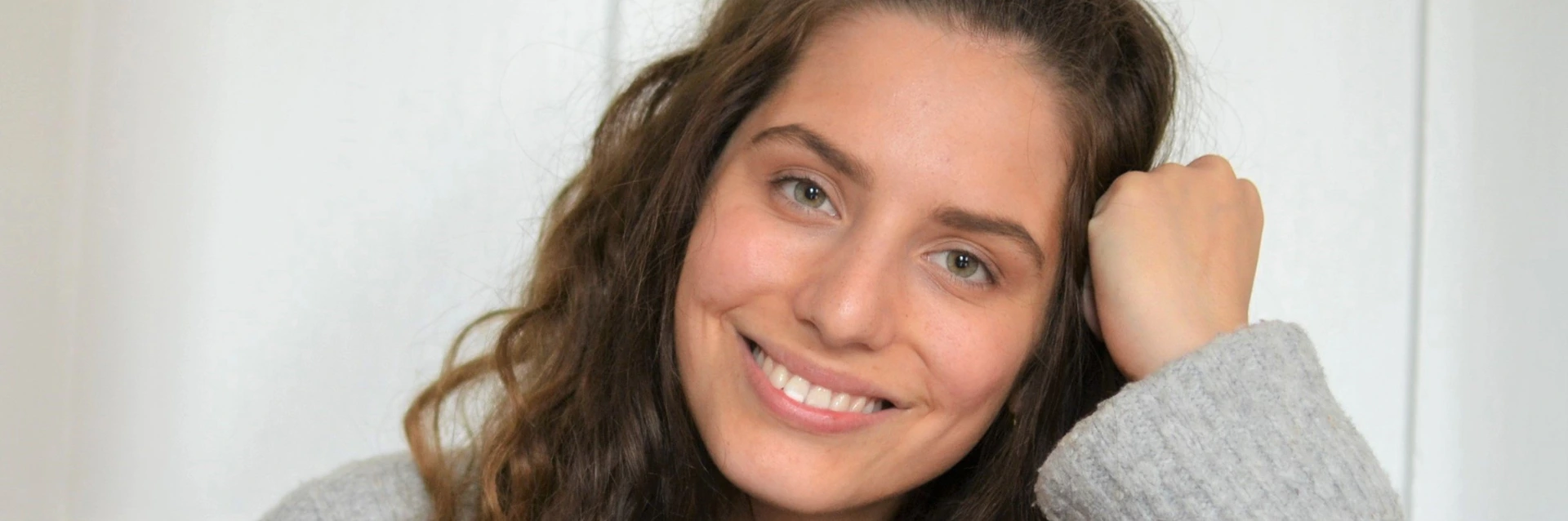 Lächelnde Frau mit braunen Locken und grauem Pullover, Porträtfoto von PALMBERG