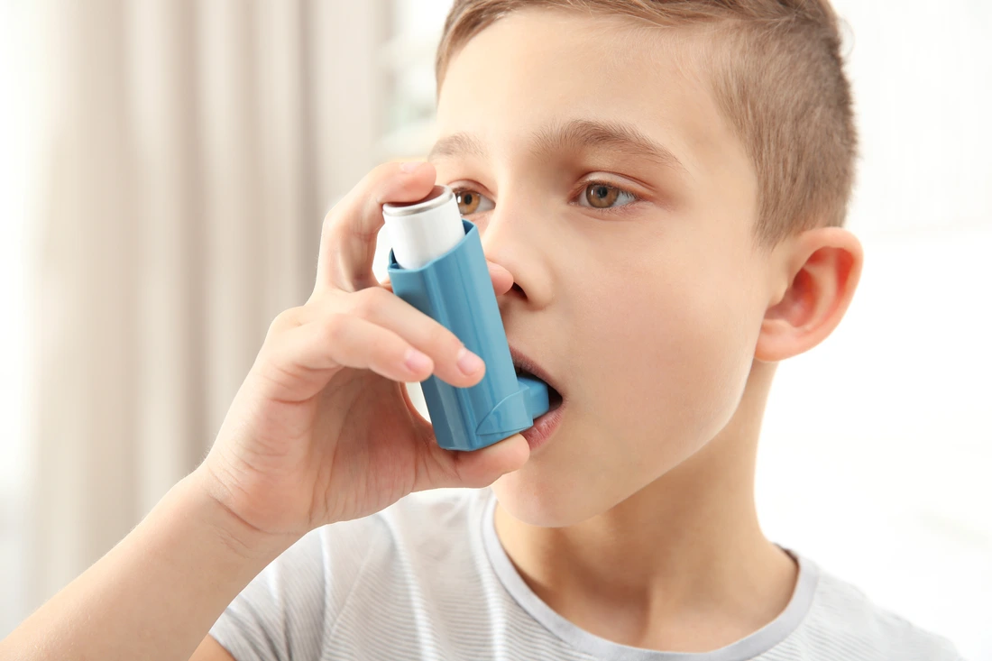 Boy using inhaler during asthmatic attack at home, closeup