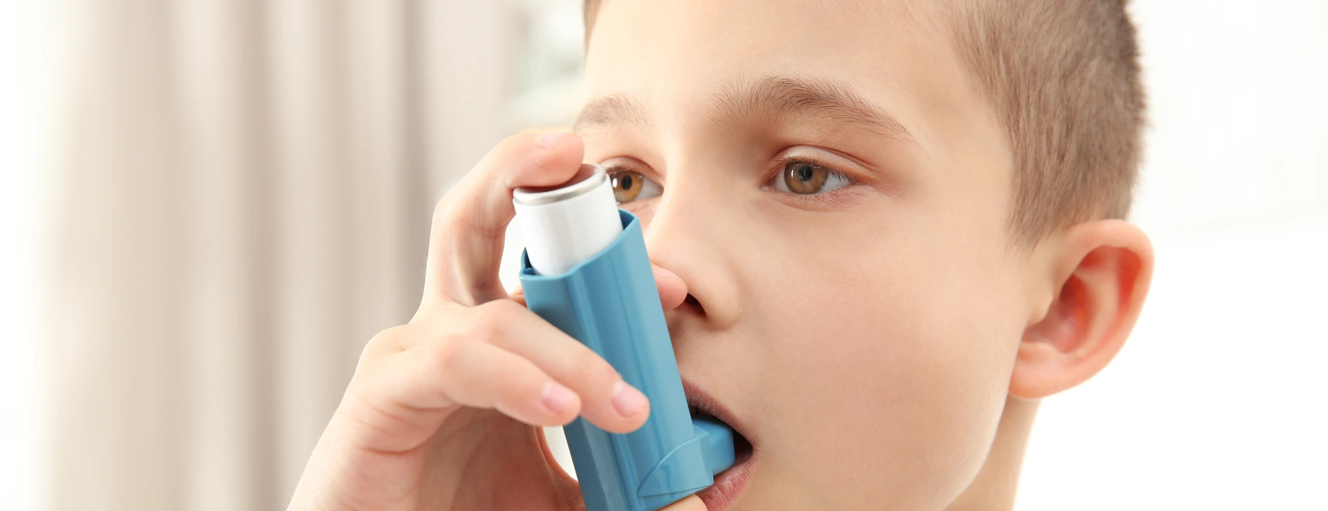 Boy using inhaler during asthmatic attack at home, closeup