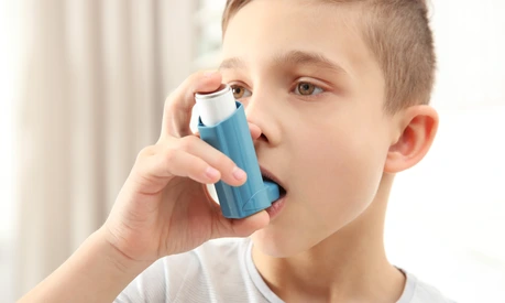 Boy using inhaler during asthmatic attack at home, closeup