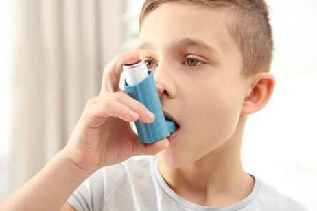 Boy using inhaler during asthmatic attack at home, closeup