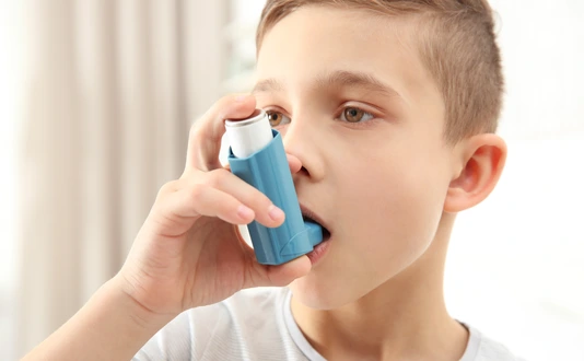 Boy using inhaler during asthmatic attack at home, closeup