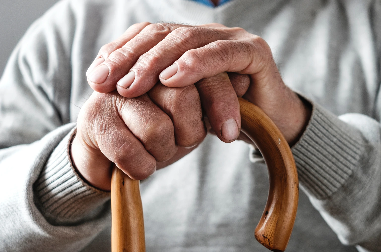 Hands of an elderly man resting on a walking cane