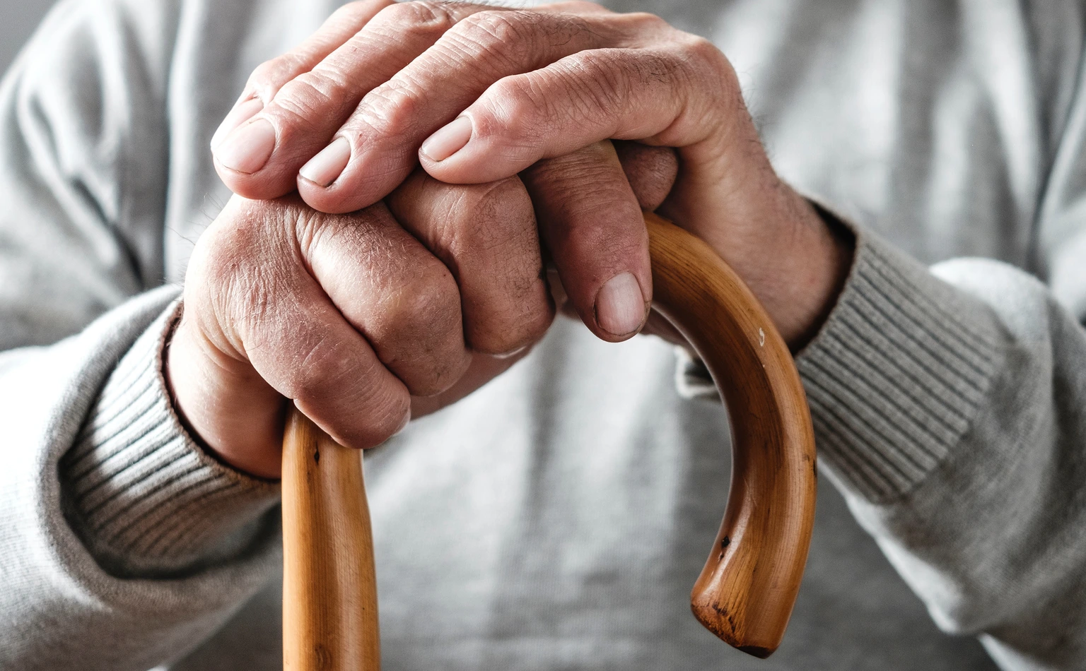 Hands of an elderly man resting on a walking cane