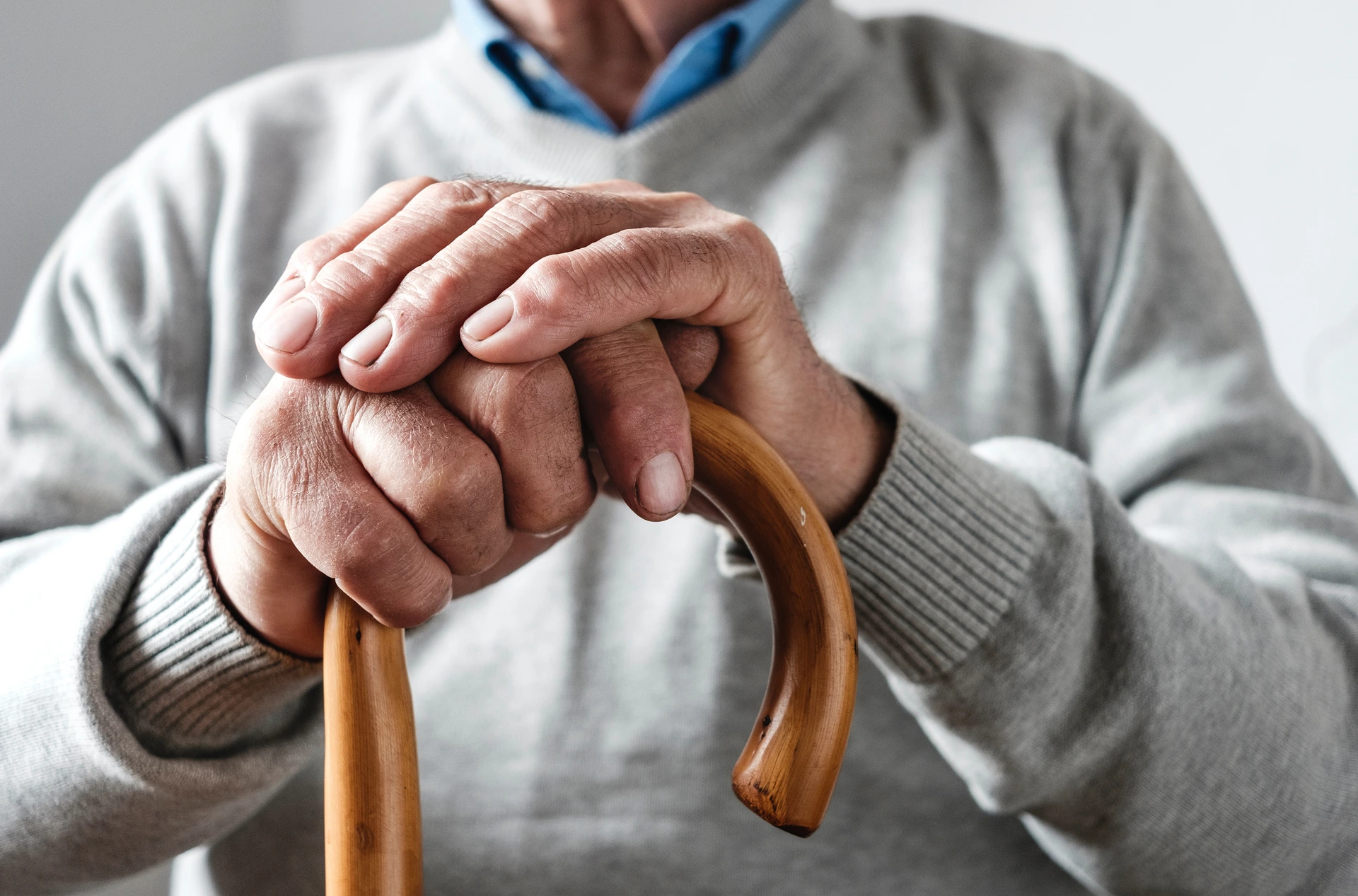 Hands of an elderly man resting on a walking cane