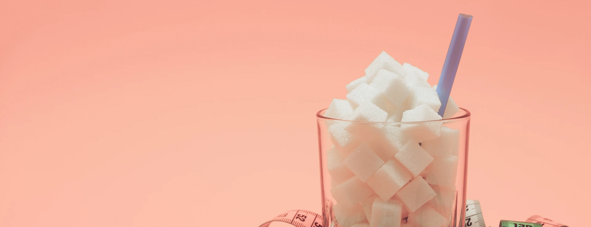 Glass full of cubes sugar with straw on a beautiful peach  background  - unhealthy diet concept.