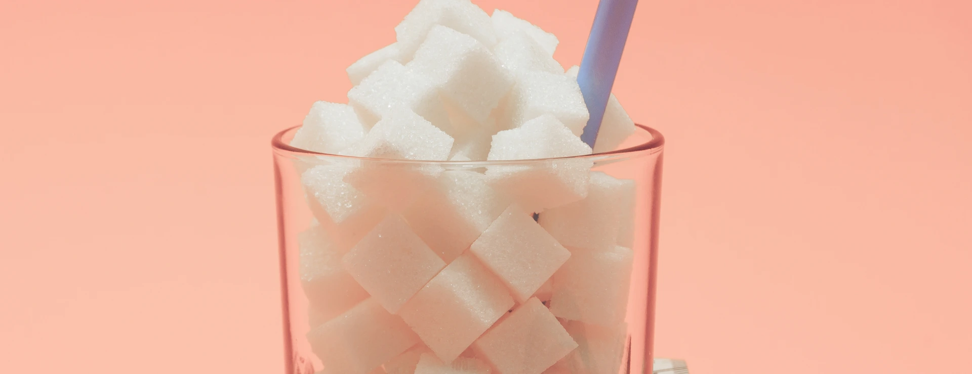 Glass full of cubes sugar with straw on a beautiful peach  background  - unhealthy diet concept.